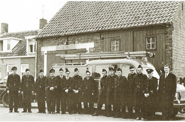 Het korps van de vrijwillige brandweer staat opgesteld voor de destijds verbouwde schuur aan het Schorretje tot brandweergarage ter gelegenheid van hun nieuwe uniformen. Naast burgemeester A. Hack staat commandant C. Boone. V.l.n.r.  B. Bliek, A. van Dalen, C.J. Moerland, P. Janse sr, W. Joosse, W. Meulmeester, C. Blaasse, P. Janse jr, K. Meerman, J. Knolle, M. Knuyt, P de Klerk en P. Meertse.